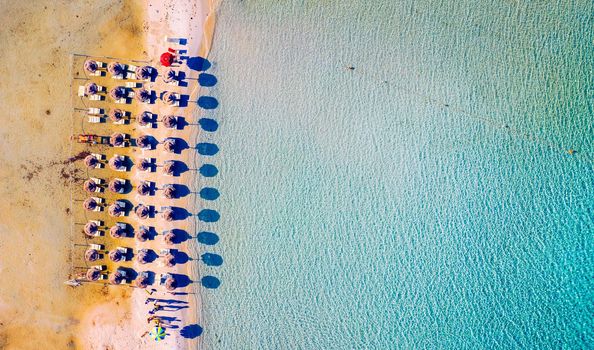 View from above, stunning aerial view of an amazing beach with beach umbrellas and turquoise clear water. Top view on sun loungers under umbrellas on the sandy beach. Concept of summer vacation. 