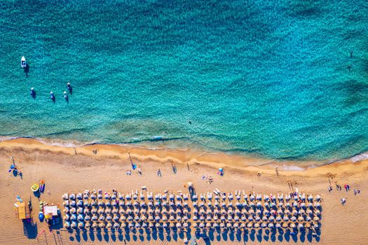 Aerial view of sandy beach with colorful umbrellas, swimming people in sea bay with transparent blue water at sunset in summer. Aerial top view on the beach, umbrellas, sand and sea waves.