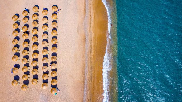 View from above, stunning aerial view of an amazing beach with beach umbrellas and turquoise clear water. Top view on sun loungers under umbrellas on the sandy beach. Concept of summer vacation. 