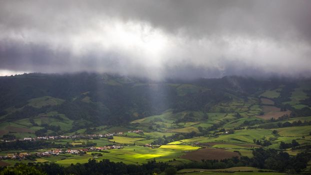 Bright sunlight shining through hole of clouds to dark scene of mountain range, Azores, Sao Miguel, Portugal. The beam of light through the dark clouds on the mountains in Azores, Portugal.