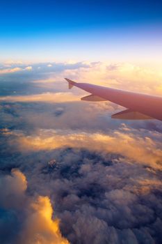 Flying and traveling, view from airplane window on the wing on sunset time. Aircraft wing under the earth and clouds. Flight in sky. Looking over aircraft wing in flight. 
