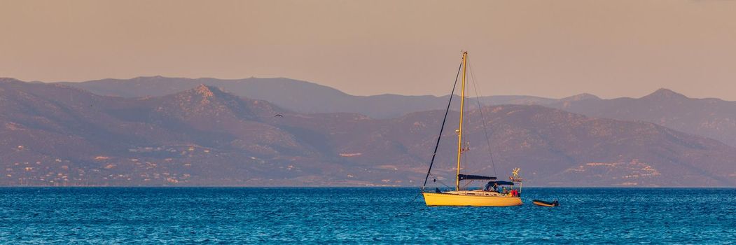 Aerial view of anchored sailing yacht in emerald sea. Aerial view of a boat. Outdoor water sports, yachting. Aerial view of anchoring yacht in open water. Ocean and sea travel and transportation