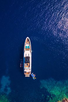 Yacht anchoring in crystal clear turquoise water in front of the tropical island, alternative lifestyle, living on a boat. Aerial view of yacht at anchor on turquoise water, showing luxury, wealth.