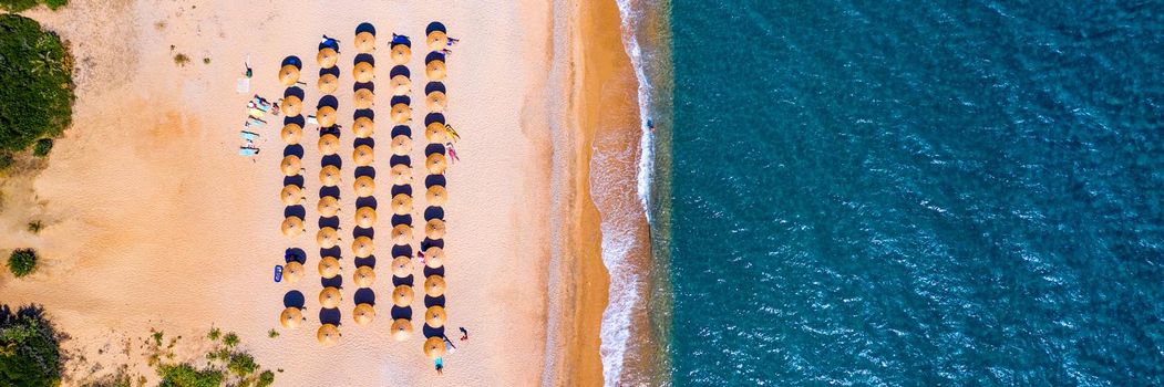 View from above, stunning aerial view of an amazing beach with beach umbrellas and turquoise clear water. Top view on sun loungers under umbrellas on the sandy beach. Concept of summer vacation. 