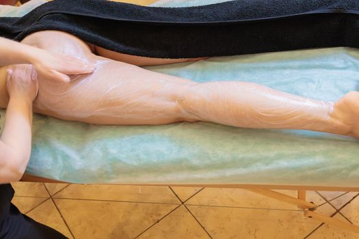 The spa master applies a scrub to the leg of a young girl. Close-up.