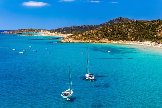 Yacht anchoring in crystal clear turquoise water in front of the tropical island, alternative lifestyle, living on a boat. Aerial view of yacht at anchor on turquoise water, showing luxury, wealth.