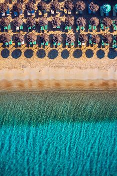 View from above, stunning aerial view of an amazing beach with beach umbrellas and turquoise clear water. Top view on sun loungers under umbrellas on the sandy beach. Concept of summer vacation. 