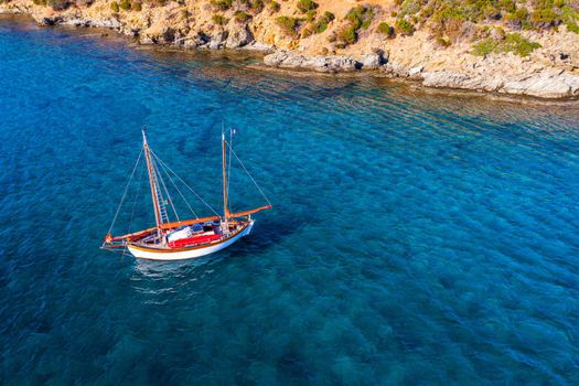 Yacht anchoring in crystal clear turquoise water in front of the tropical island, alternative lifestyle, living on a boat. Aerial view of yacht at anchor on turquoise water, showing luxury, wealth.