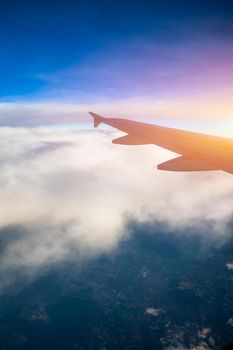 Flying and traveling, view from airplane window on the wing on sunset time. Aircraft wing under the earth and clouds. Flight in sky. Looking over aircraft wing in flight. 
