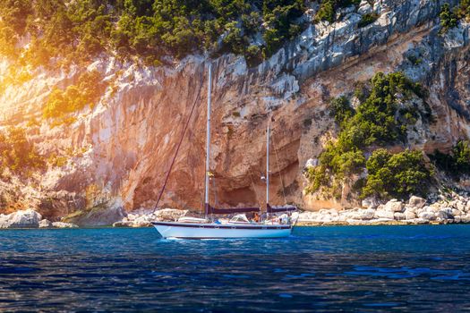 Yacht anchoring in crystal clear turquoise water in front of the tropical island, alternative lifestyle, living on a boat. Aerial view of yacht at anchor on turquoise water, showing luxury, wealth.