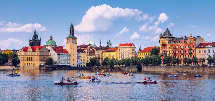 Scenic embankment in Prague city with paddle boats on Vltava river and Charles bridge; Historical center of Prague, buildings and landmarks of old town, Prague, Czech Republic