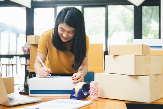 Closeup hand of young woman writing address on parcel box  for delivery order to customer, shipping and logistic, merchant online and seller, business owner or SME, online shopping.
