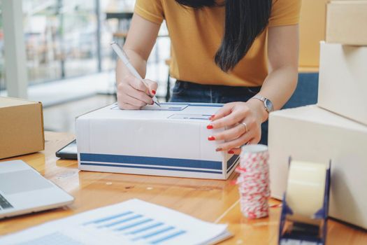 Closeup hand of young woman writing address on parcel box  for delivery order to customer, shipping and logistic, merchant online and seller, business owner or SME, online shopping.
