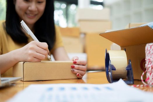 Closeup hand of young woman writing address on parcel box  for delivery order to customer, shipping and logistic, merchant online and seller, business owner or SME, online shopping.
