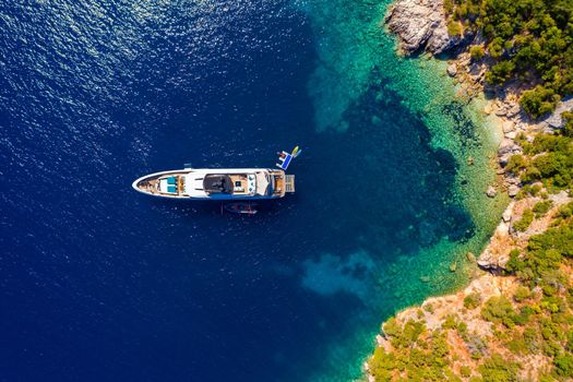 Aerial view of anchored sailing yacht in emerald sea. Aerial view of a boat. Outdoor water sports, yachting. Aerial view of anchoring yacht in open water. Ocean and sea travel and transportation