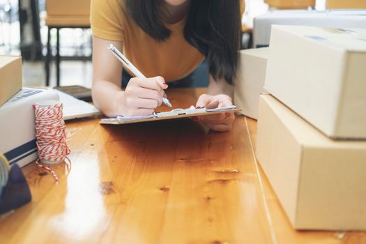 Young business startup online seller owner using computer for checking the customer orders from email or website and preparing packages for product office equipment.