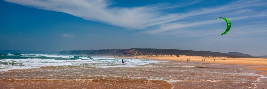 Surfers in Praia da Bordeira beach near Carrapateira, Portugal. Kiteboarder kitesurfer athlete performing kitesurfing kiteboarding tricks. Praia da Bordeira is popular location for surfing. Portugal