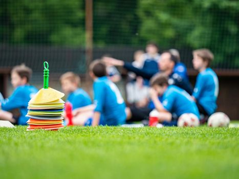 Soccer players rest  sitting between cone markers on green artificial turf for soccer training.