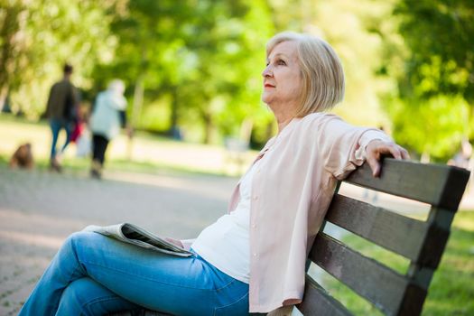 Adult woman sitting in park and reading newspapers.