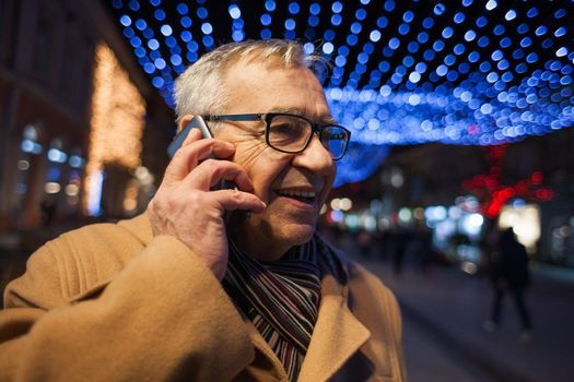Outdoor portrait of happy senior man in city. He is talking on phone.