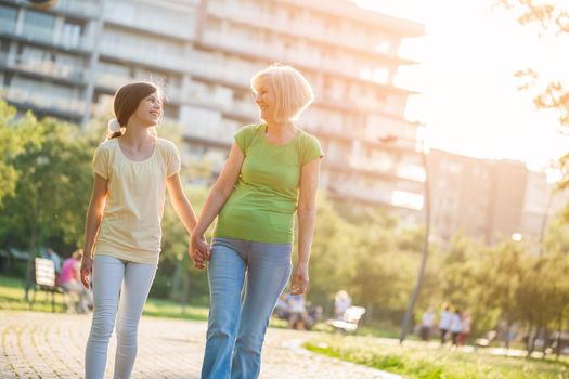 Grandmother and granddaughter are walking in park in summer.