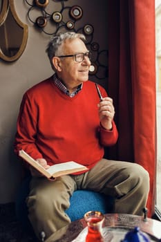 Senior man is sitting in cafe and reading a book.