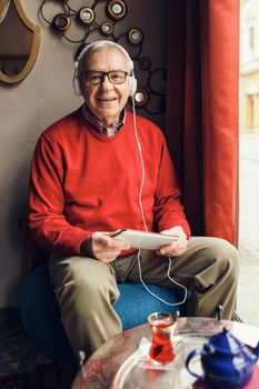 Portrait of happy senior man who is chatting on digital tablet in a cafe.