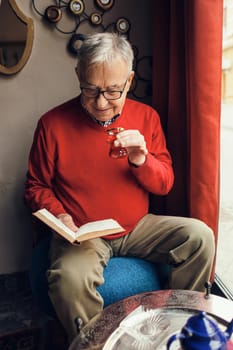 Senior man is sitting in cafe and reading a book.