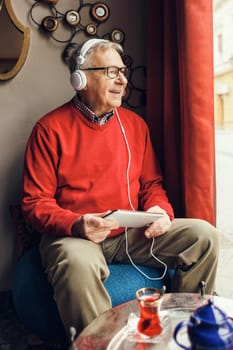 Portrait of happy senior man who is chatting on digital tablet in a cafe.