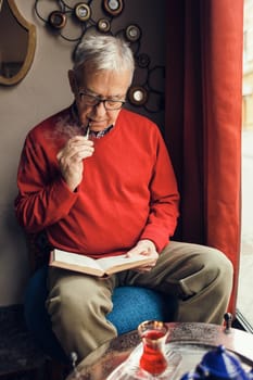 Senior man is sitting in cafe and reading a book.