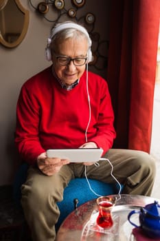 Portrait of happy senior man who is chatting on digital tablet in a cafe.