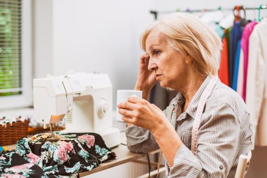 Adult woman is sewing in her studio. She is tired.