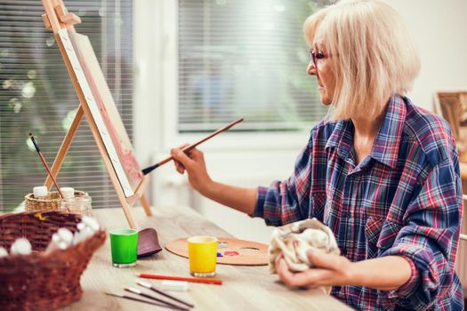 Elderly woman is painting in her home. Retirement hobby.