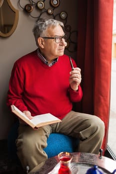 Senior man is sitting in cafe and reading a book.