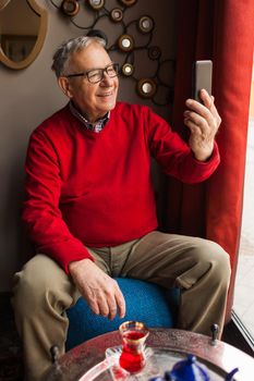 Portrait of senior man who is taking selfie in a cafe.