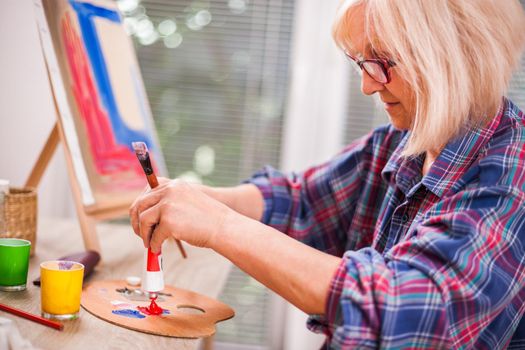 Elderly woman is painting in her home. Retirement hobby.