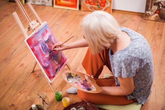 Elderly woman is painting in her home. Retirement hobby.