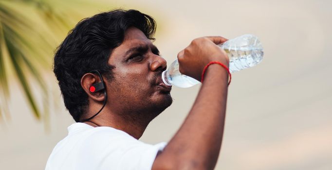 Close up Asian young sport runner black man wear athlete headphones he drinking water from a bottle after running at the outdoor street health park, healthy exercise workout concept