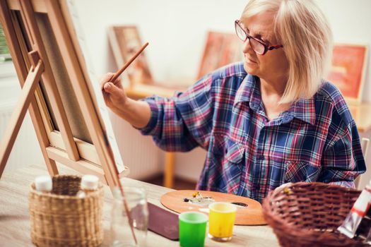 Elderly woman is painting in her home. Retirement hobby.