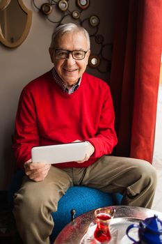 Portrait of happy senior man who is using digital tablet in a cafe.