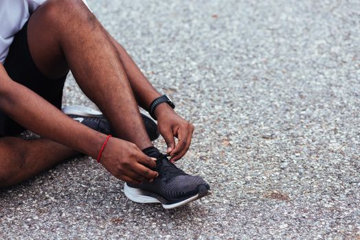 Close up Asian sport runner black man sitting shoelace trying running shoes getting ready for jogging and run at the outdoor street, health exercise workout concept