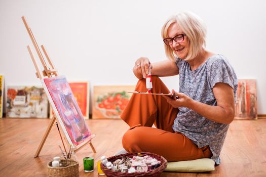 Elderly woman is painting in her home. Retirement hobby.