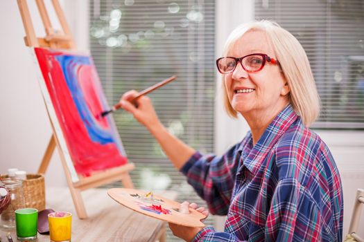 Elderly woman is painting in her home. Retirement hobby.