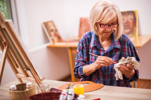 Elderly woman is painting in her home. Retirement hobby.