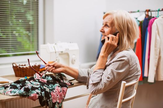 Adult woman is sewing in her studio. She is talking with client.