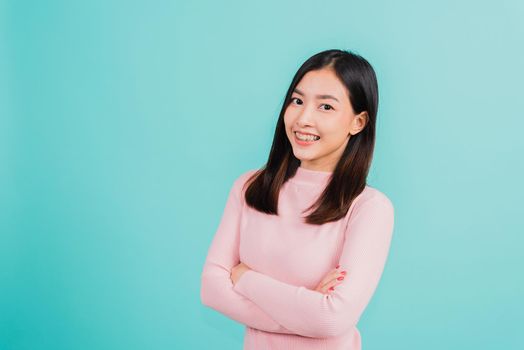 Young Asian beautiful woman smiling wear silicone orthodontic retainers on teeth with crossed arms, studio isolated on blue background, retaining tools after removable braces. Dental hygiene concept