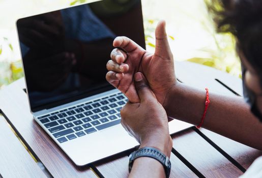 Closeup hands the Asian black man holding his wrist pain from using laptop computer he working long time, Injury office syndrome hand pain by occupational disease concept