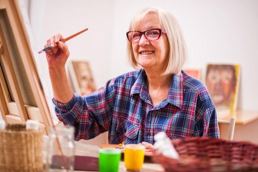 Elderly woman is painting in her home. Retirement hobby.