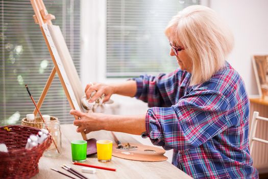 Elderly woman is painting in her home. Retirement hobby.