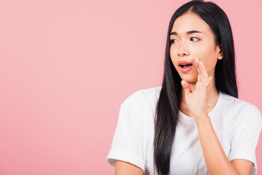 Asian happy portrait beautiful cute young woman teen standing hand on mouth talking whisper secret rumor studio shot isolated on pink background, Thai female looking to side away with copy space